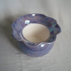 May include: A small, iridescent blue ceramic planter with a scalloped rim. The planter has a white interior and is perfect for small plants.