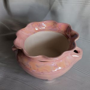 May include: A pink ceramic planter with a scalloped rim and a glazed finish. The planter has a light pink and white marbled design.