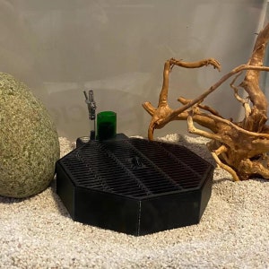 Può includere: Filtro per acquario ottagonale nero con una pietra d'aria verde e una pompa d'aria argentata. Il filtro è posto su un substrato di ghiaia bianca.