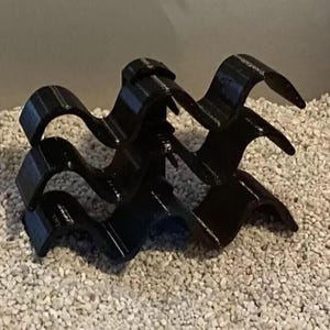May include: Three black plastic wavy shelf brackets stacked on top of each other. The brackets are designed to support shelves.
