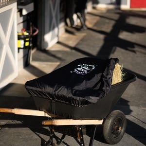May include: A black wheelbarrow with a black cover and a bale of hay inside. The cover has the text "Wheelbarrow Covers" printed on it.