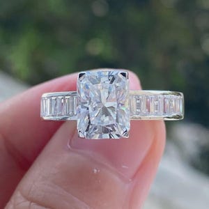 May include: A silver engagement ring with a large, rectangular, clear diamond center stone and a band of smaller, baguette-shaped diamonds.