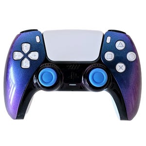 May include: A black PlayStation 5 DualSense controller with a purple and blue iridescent finish. The controller has blue thumbsticks and white buttons.
