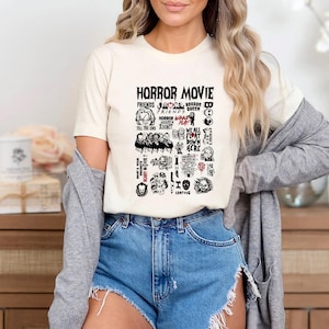 Peut inclure: T-shirt cr&egrave;me avec un motif graphique comportant les mots "HORROR MOVIE" et diverses ic&ocirc;nes et phrases sur le th&egrave;me de l'horreur en noir et rouge. Le t-shirt est port&eacute; avec un short en jean.