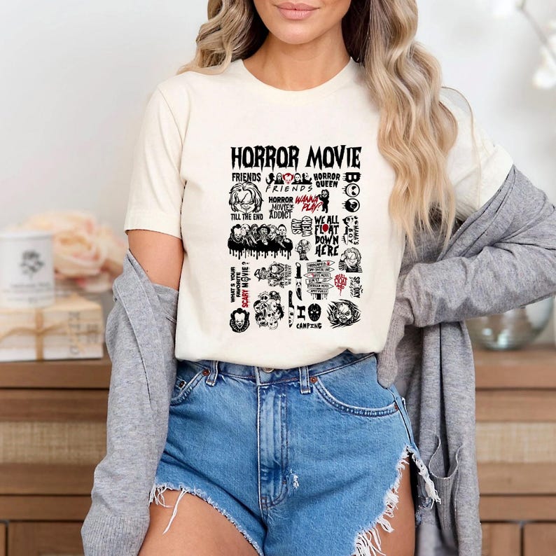 Peut inclure: T-shirt cr&egrave;me avec un motif graphique comportant les mots "HORROR MOVIE" et diverses ic&ocirc;nes et phrases sur le th&egrave;me de l'horreur en noir et rouge. Le t-shirt est port&eacute; avec un short en jean.