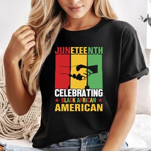 Peut inclure: T-shirt noir avec l'inscription "JUNETEENTH CELEBRATING BLACK AFRICAN AMERICAN" en rouge, jaune et vert. Le motif comprend une poignée de main. Le t-shirt est porté par une personne.