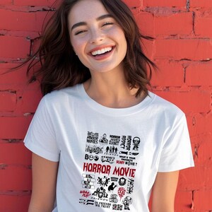 Peut inclure: T-shirt blanc avec un motif graphique comportant les mots "HORROR MOVIE" en grandes lettres rouges. Le motif comprend diverses images et phrases sur le th&egrave;me de l'horreur comme "HORROR ADDICT" et "SCARY MOVIE?"