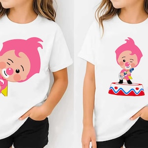 May include: White t-shirts with a cartoon clown design. One shirt shows the clown peeking from behind a yellow shape, the other shows the clown on a circus platform. The clown has pink hair and a red nose.