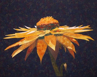 Op de afbeelding: Een gequilt kunstwerk met een grote, gestileerde gele en oranje bloem tegen een donkerblauwe achtergrond. De bloemblaadjes zijn gelaagd en het midden is een mix van bruin en groen. De achtergrond heeft een wervelend patroon.