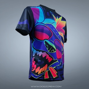 May include: A black short-sleeved t-shirt featuring a colourful graphic print of a cartoon dog wearing sunglasses. The dog's face is in a fierce expression with its mouth open and teeth showing. The background is a mix of geometric shapes and lines in bright colours.