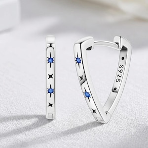 Peut inclure: Une paire de boucles d'oreilles créoles en argent de forme triangulaire. Les boucles d'oreilles présentent des motifs d'étoiles gravés, certaines étoiles étant incrustées de petites pierres bleues. Le texte S925 est gravé à l'intérieur.