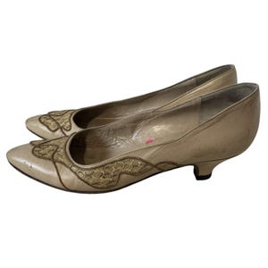 Può includere: Un paio di scarpe con tacco in pelle beige con punta a punta. Le scarpe hanno un motivo decorativo sul davanti, realizzato in una tonalità di pelle beige diversa.