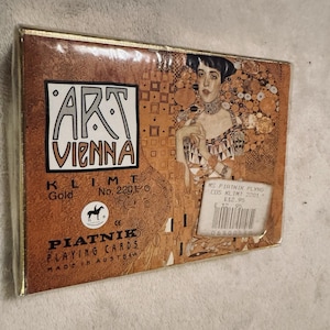Puede incluir: Baraja de cartas Piatnik, con un diseño dorado y marrón con el texto "ART VIENNA" y una imagen de una mujer. Las cartas son Klimt No. 2201, fabricadas en Austria.
