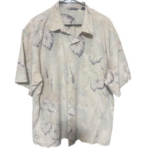 Op de afbeelding: Een shirt met korte mouwen met een tropisch bladerpatroon in crème, beige en grijstinten. Het shirt heeft een kraag, een borstzak en hangt aan een zwarte hanger. De merknaam "Robbie" is zichtbaar op de kraag.