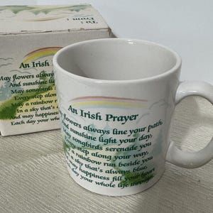 May include: White ceramic mug with a green and rainbow design. The mug has a quote that reads "An Irish Prayer: May flowers always line your path, and sunshine light your day, May songbirds serenade you, Every step along your way, A rainbow run beside you, In a sky that's always blue, May happiness fill your heart, Each day your whole life through."
