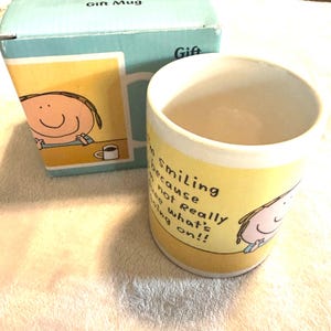 Op de afbeelding: Een keramische cadeau mok met een gele achtergrond en de tekst "I'm Smiling because not Really what's going on!!". De mok heeft een cartoon tekening van een lachende persoon. De mok wordt geleverd met een bijpassende doos.