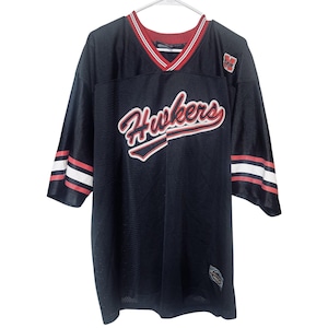 Puede incluir: Camiseta de malla negra con la palabra "Hawkers" en escritura roja y blanca en el pecho. La camiseta tiene un cuello y detalles de manga a rayas rojas y blancas. Un pequeño parche con el logotipo está en la parte superior derecha del pecho.