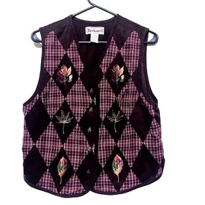 Puede incluir: Un chaleco marrón con estampado de cuadros y bordado floral. El chaleco tiene cuello en V y está hecho de una tela suave y acolchada. La etiqueta del chaleco dice "Bechmel".