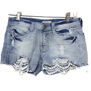 May include: Light blue denim shorts with a white crochet trim. The shorts have distressed details and a button fly.