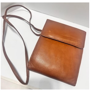 May include: A rectangular brown leather crossbody bag with a smooth finish and a fold-over flap closure. The bag features a thin, matching brown leather shoulder strap attached to the sides, providing a simple and functional design for carrying items.