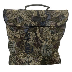 May include: A vintage tapestry briefcase with a black handle and trim. The fabric features a repeating pattern of travel-related text and logos in shades of blue, green, and brown. The briefcase has a clasp closure.