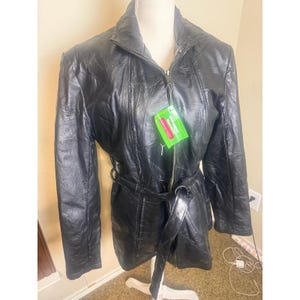 May include: A black leather jacket featuring a full-length front zipper, a high collar, and a matching tie belt at the waist. The jacket is constructed from multiple stitched panels and includes a green rectangular tag with the text Giovanni Savare.