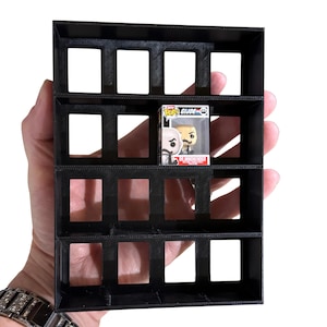 May include: Black, multi-compartment display shelf, designed to hold small collectibles. One compartment contains a Funko Pop figure. The shelf is held in a person's hand against a white background. The Funko Pop figure is of the character Dr. Mindbender from G.I. Joe.