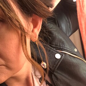 May include: A gold-colored chain earring with a large, iridescent crystal pendant. The crystal reflects multiple colors. The earring is dangling near a person's ear. The person is wearing a black leather jacket.