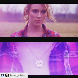 Może przedstawiać: Kobieta w czerwono-czarnej koszuli w kratę i srebrnym naszyjniku. Naszyjnik ma okrągłą zawieszkę z wygrawerowanymi cyframi "606". Tło to rozmyta scena na zewnątrz z fioletowym odcieniem.