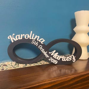 May include: A dark grey infinity symbol with the names "Karolina" and "Marius" and the date "5th October 2019" written in white.