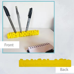 May include: A bright yellow pen holder with the name "MRS NORMAN" in capital letters. Three pens are in the holder. The back of the holder has the text "THANKS FOR HELPING ME GROW".