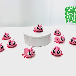 May include: A collection of small pink cartoon-style ant figurines with large white eyes and red feet, arranged around a white cylindrical base. The green text KIKO PRINT is visible in the upper right corner of the image.