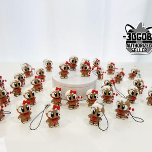 May include: A collection of small, brown gingerbread man figurines with white frosting, red bowties, and black eyes. Some hold candy canes. Each has a black lanyard. The figurines are on a white surface, with a logo that says "-3DGOB- AUTHORIZED SELLER".