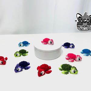 May include: A collection of small, multi-colored 3D printed turtle figurines in shades of red, blue, green, and purple, arranged around a central white circular platform. A black and white logo reads 3DGOB AUTHORIZED SELLER.