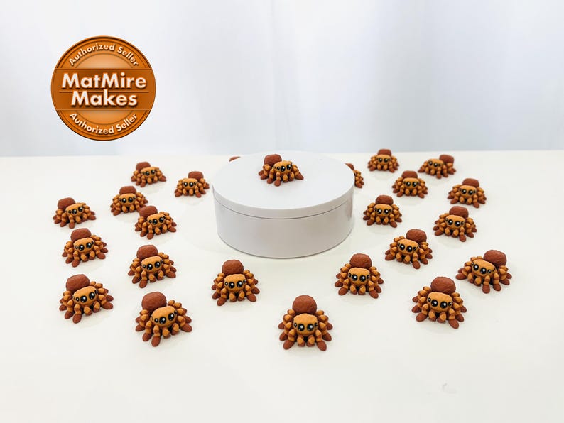 May include: A collection of miniature spider figurines, each with a brown body, lighter brown abdomen, and a dark brown head. The spiders are arranged around a white, circular platform. The image includes a logo.