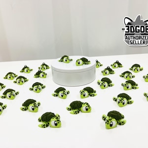 May include: A collection of small, green turtle-shaped charms with dark green shells and light green bodies. The charms are scattered on a white surface, some are on a white platform. The image includes a seller's logo.
