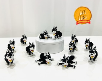 May include: A collection of black and white dog figurines with red collars and yellow tags. Some dogs are standing, while others are lying down. The figurines are arranged on a white surface, with an "Art Flex" logo in the background.