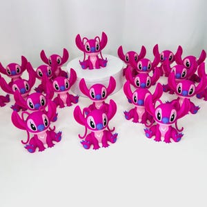 May include: A group of 15 pink Stitch figurines with blue accents. The Stitch figurines are arranged in a circle on a white surface.