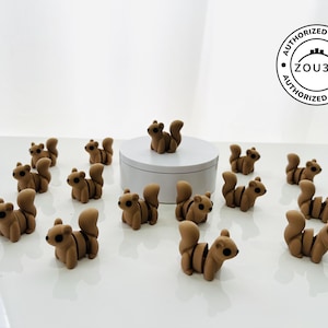 May include: A collection of small, brown squirrel figurines with tan stripes and fluffy tails. The squirrels have black eyes and are arranged on a white surface. A white platform holds one squirrel. The image includes a "ZOU3D" logo.