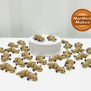 May include: A collection of 20 small, brown, ceramic animal figurines. The figurines are shaped like otters and are arranged in a circle on a white surface. The figurines are all facing the same direction and have a similar design.