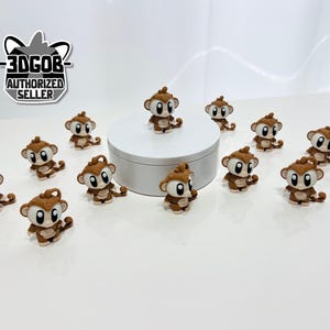 May include: A collection of small, brown monkey figurines with large, expressive eyes. The monkeys are arranged on a white surface, some sitting and others standing. The text "-3DGOB- AUTHORIZED SELLER" is visible in the upper left corner.