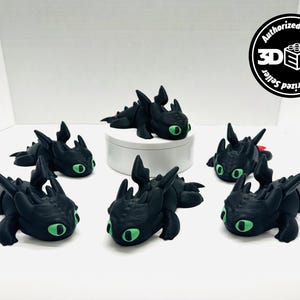 May include: A collection of black dragon figurines with green eyes and red accents. The figurines are in various poses, some lying down, others upright. The background is white, and the figurines are the primary focus.