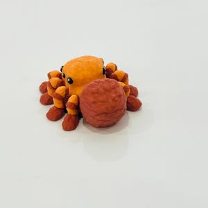 May include: A 3D-printed orange octopus figurine with dark eyes and reddish-orange tentacles. The octopus is holding a textured, reddish-brown sphere. The figurine is set against a plain white background.