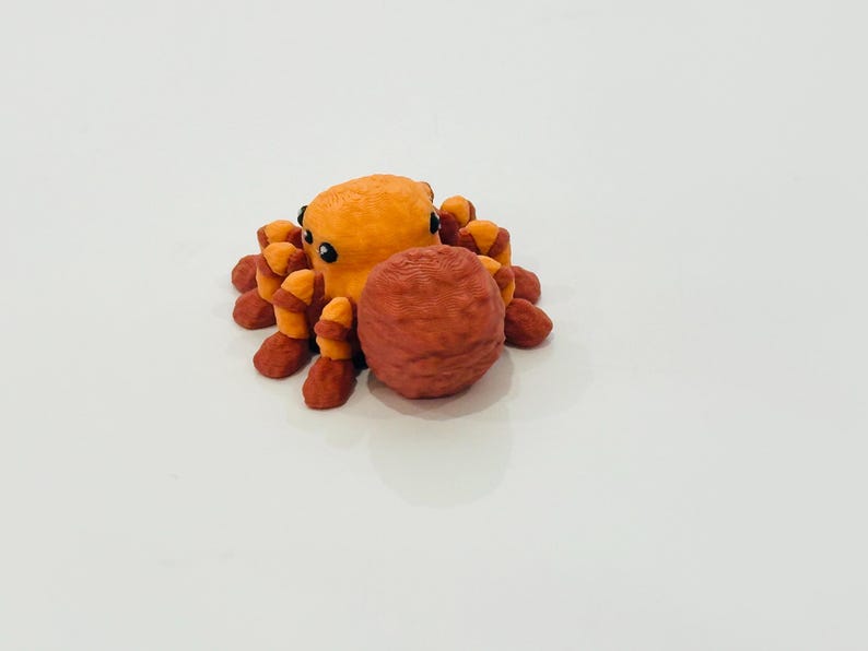 May include: A 3D-printed orange octopus figurine with dark eyes and reddish-orange tentacles. The octopus is holding a textured, reddish-brown sphere. The figurine is set against a plain white background.