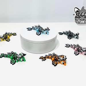 May include: A collection of colorful, miniature dragon figurines. The dragons are in various colors, including yellow, green, orange, pink, blue, and gray, with black accents. The figurines are displayed on a white surface.