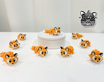 May include: Orange and white fox figurines with black accents are displayed on a white surface. One fox is on a white pedestal. The figurines have large eyes and are in various poses. A sticker with the text "-3DGOB- AUTHORIZED SELLER" is in the background.