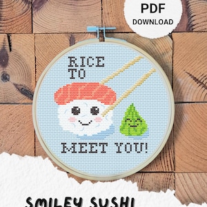 Puede incluir: Un patrón de punto de cruz en un aro de madera presenta un personaje de sushi sonriente con palillos y un personaje de wasabi. También se incluye el texto "RICE TO MEET YOU!" y "SMILEY SUSHI CROSS STITCH PATTERN".