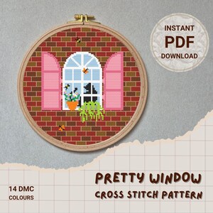 May include: A cross-stitch pattern of a window scene, framed in a wooden hoop. The design features a brick wall, pink window frames, and a white arched window with a flower pot and greenery. The text "PRETTY WINDOW CROSS STITCH PATTERN" is displayed.