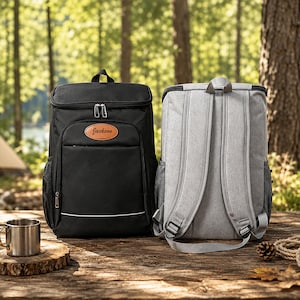May include: A black backpack with a tan oval patch featuring the name Jackson and a light grey backpack with adjustable shoulder straps. Both backpacks feature a rectangular shape, top carry handles, side mesh pockets, and silver-tone zippers.
