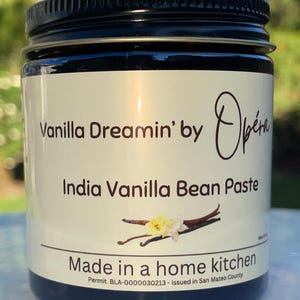May include: A black jar with a white label that reads "Vanilla Dreamin' by Opéra India Vanilla Bean Paste Made in a home kitchen Permit BLA-0000030213 - Issued in San Mateo County".